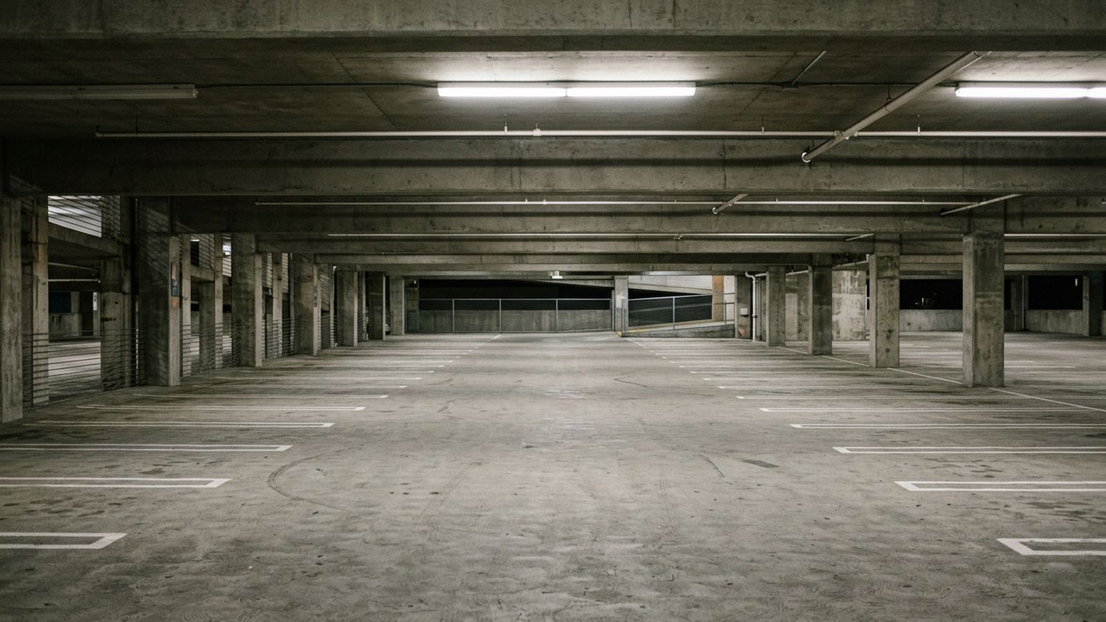 The interior of a plain concrete parking deck with empty marked bays, painted floor lines and overhead lighting, no vehicles or people in frame